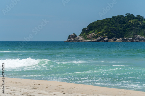 Grumari beach near Barra da Tijuca in Rio de Janeiro, Brazil. Sunny day with blue sky, clear water and small waves. Hills and nature around