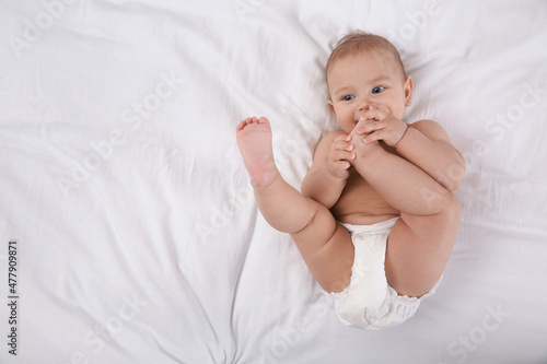 Cute baby in dry soft diaper on white bed, top view. space for text