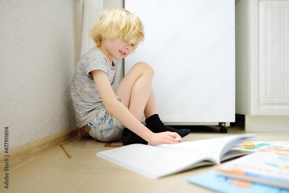 Elementary student boy doing homework on a floor at home. Child learning, doing exercises in workbook. Math and language tutorial. Preparing preschooler baby for school. Elementary student boy doing homework on a floor at home. Child learning, doing exercises in workbook. Math and language tutorial. Preparing preschooler baby for school.