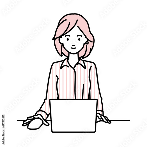 デスクで座ってPCを使っているブラウスの女性