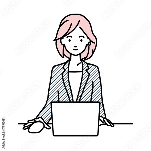 デスクで座ってPCを使っているスーツの女性