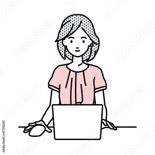 デスクで座ってPCを使っているオフィスカジュアルの女性