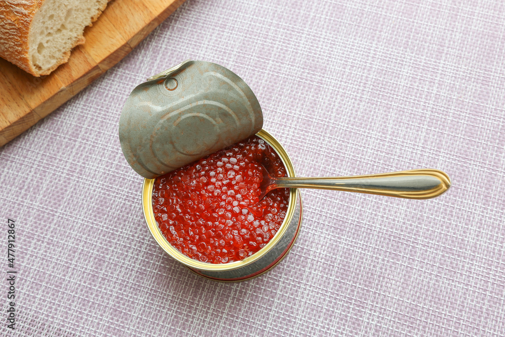 Fototapeta premium Caviar is in a jar. Close-up of red caviar and a spoon. In the background there is bread.