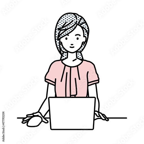 デスクで座ってPCを使っているオフィスカジュアルの女性