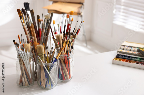 Different brushes and paints on white table in studio, space for text. Artist's workplace