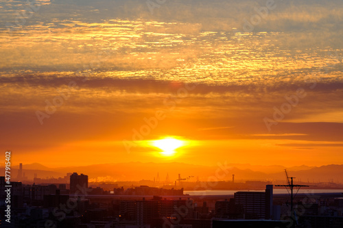 早朝、日が昇りあたりはオレンジ色に染まる。雲に隠れていた太陽が顔を出す。大阪湾の先に和泉山脈・紀伊山地の稜線が見える。