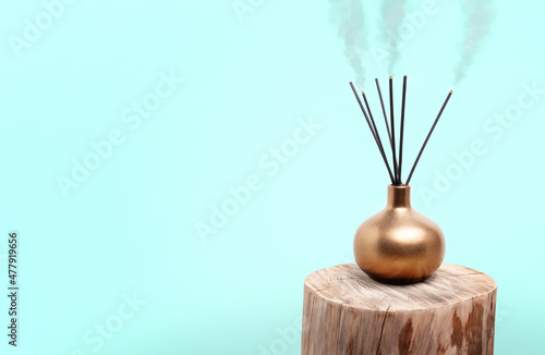 Incense holder with burning incense sticks placed on wood log. Gold incense vase or incense burner with light blue background. Used during meditation, religious practice or freshen up the scents.