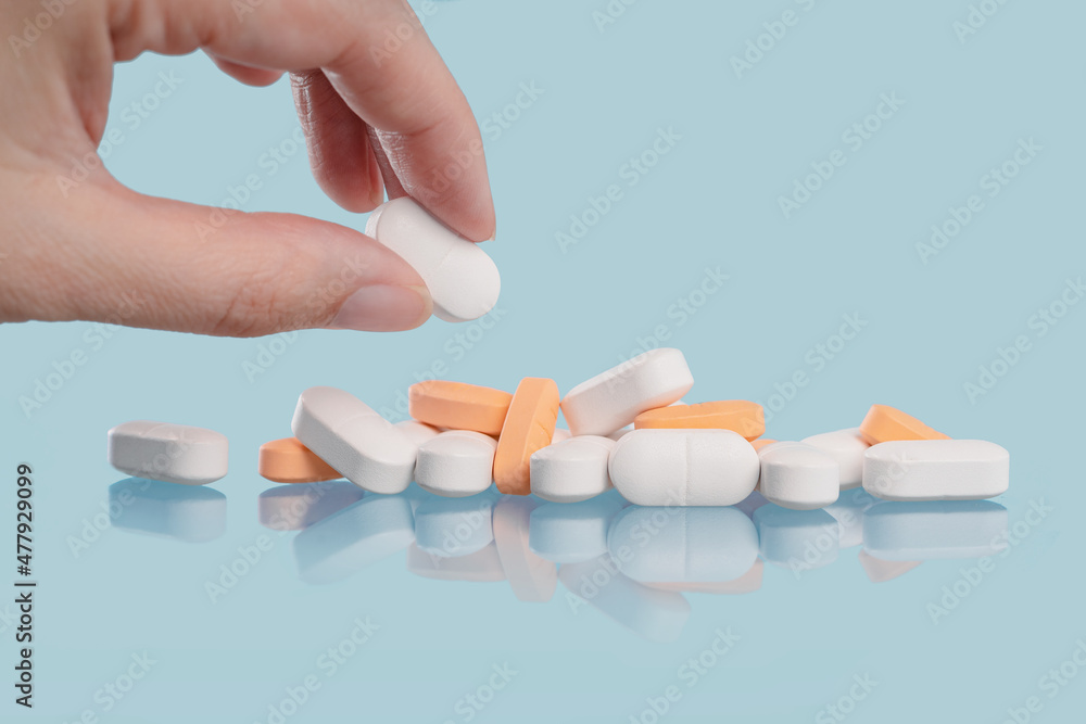 Medical background. Hand holds one of many capsule tablets or pills on blue table. Close up. Healthcare pharmacy and medicine concept with copy space Painkillers or prescription drugs consumption Medical background. Hand holds one of many capsule tablets or pills on blue table. Close up. Healthcare pharmacy and medicine concept with copy space Painkillers or prescription drugs consumption