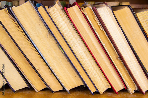 Old stack of books on the bookshelf. Old books in a row. Book binding. Bookshelf. Yellow paper pages. Literary edition. Background image. Free space for text.