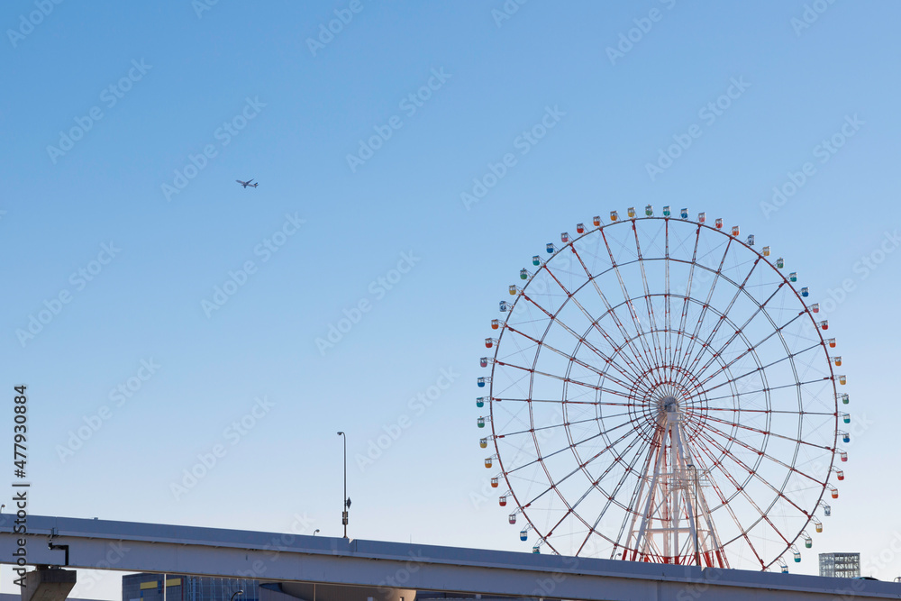 青空を背景にカラフルな観覧車と上空を通過する飛行機