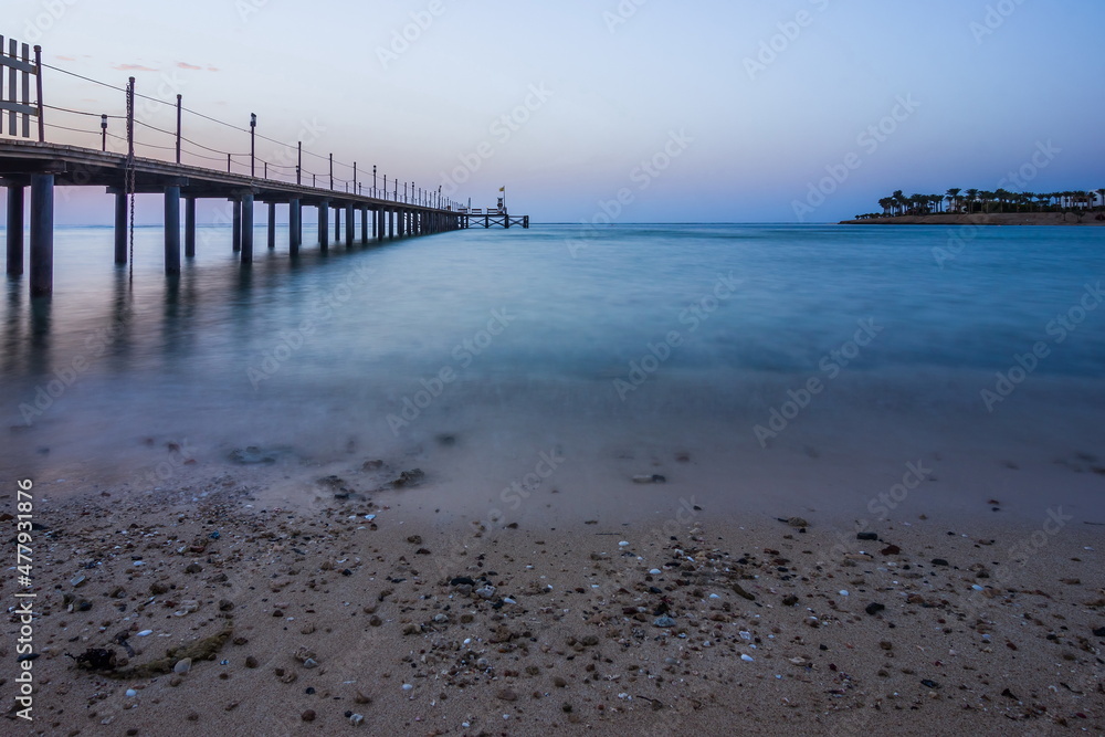 Wooden pier at sunrise in the tropical sea. Palm trees in the di