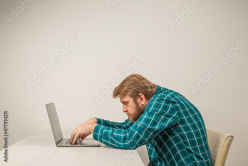 Beard emotional man in slouching position sitting in office room, working with laptop photo