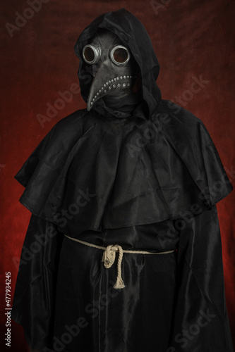 Фотография Dark black figure of a man in a mask of plague doctor stands on red background