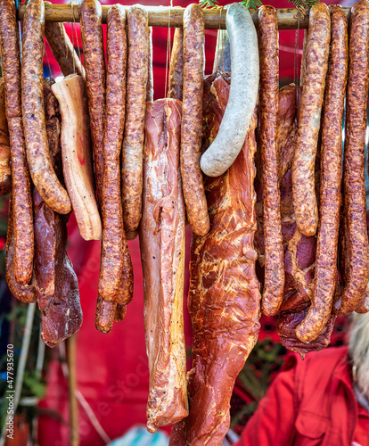 Many smoked Sausages and other pork meat products hanging from a stick at a food festival.