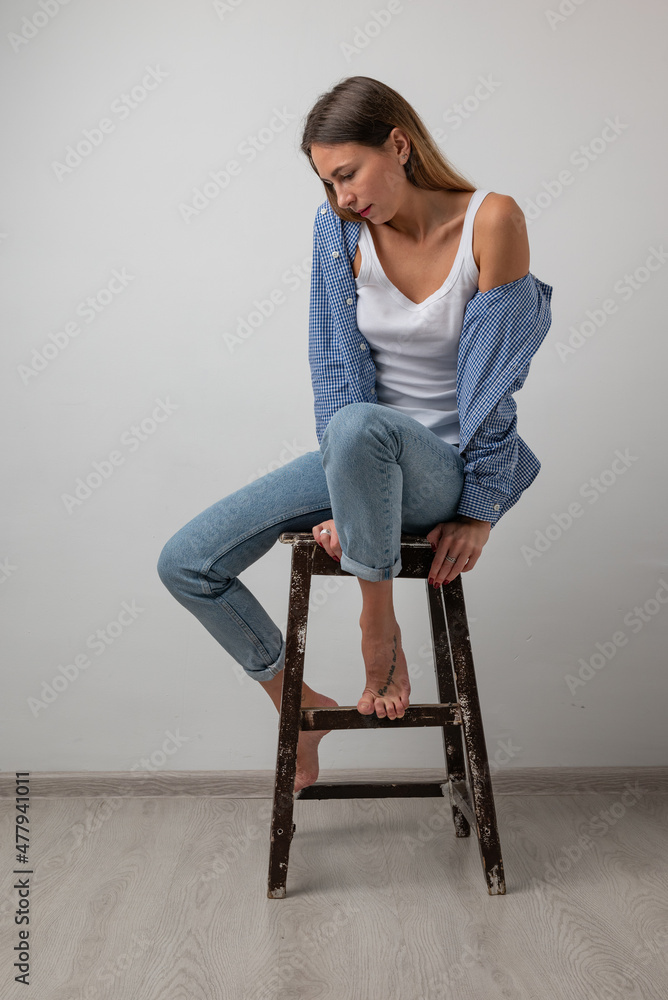 beautiful girl in a white t-shirt, blue jeans sitting on a chair , smiling and posing beautiful girl in a white t-shirt, blue jeans sitting on a chair , smiling and posing