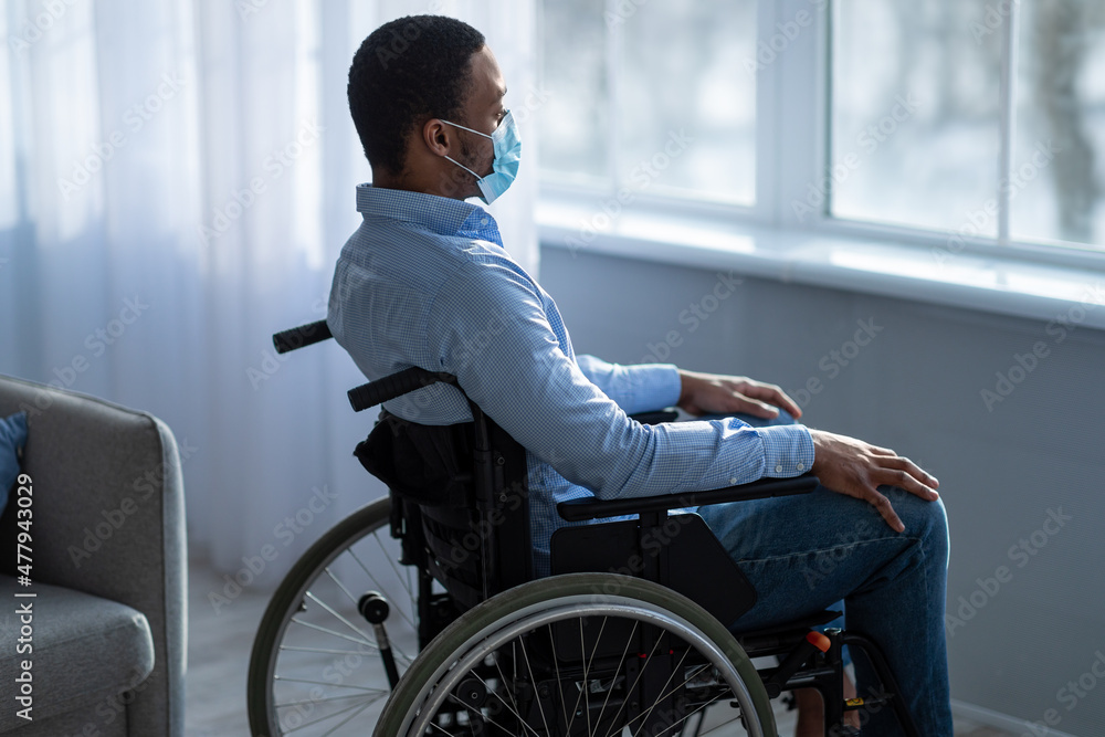 Impaired black guy in face mask suffering from depression at home during covid lockdown Impaired black guy in face mask suffering from depression at home during covid lockdown
