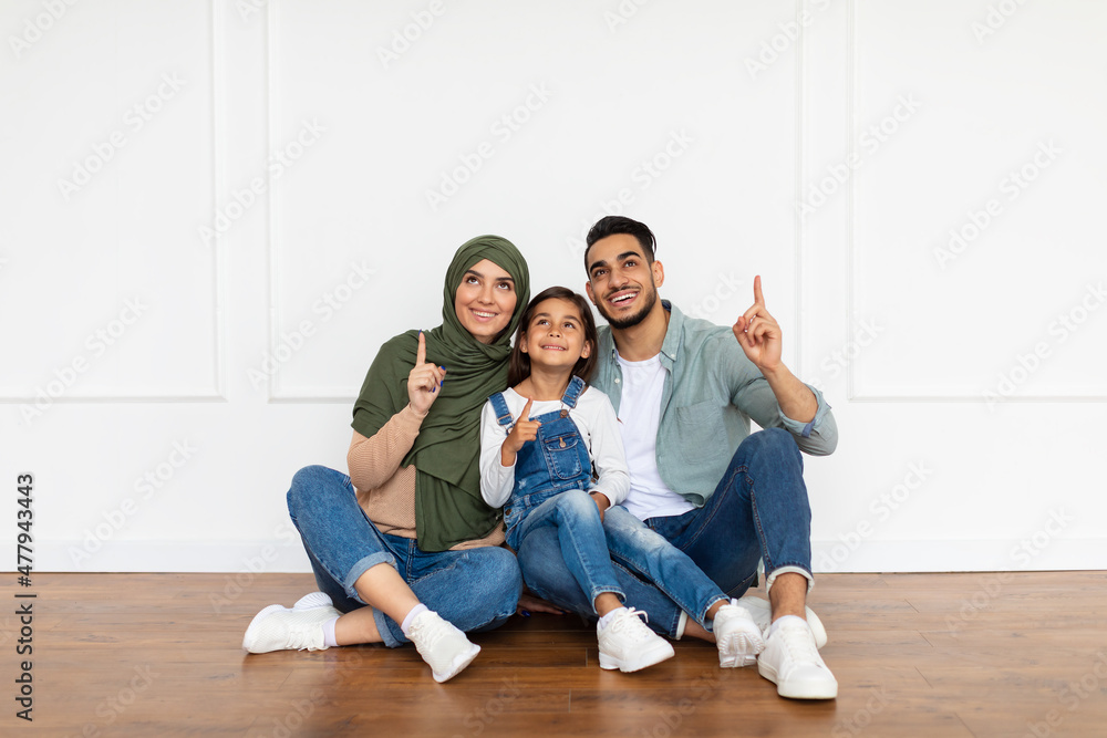 Happy man, woman and girl pointing fingers up at home Happy man, woman and girl pointing fingers up at home