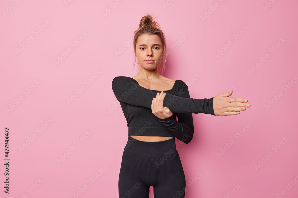 Fitness woman in black tracksuit warms up before workout stretches arms leads sporty lifestyle motivates you to do sport isolated over pink background. Athletic female model exercises indoor Fitness woman in black tracksuit warms up before workout stretches arms leads sporty lifestyle motivates you to do sport isolated over pink background. Athletic female model exercises indoor