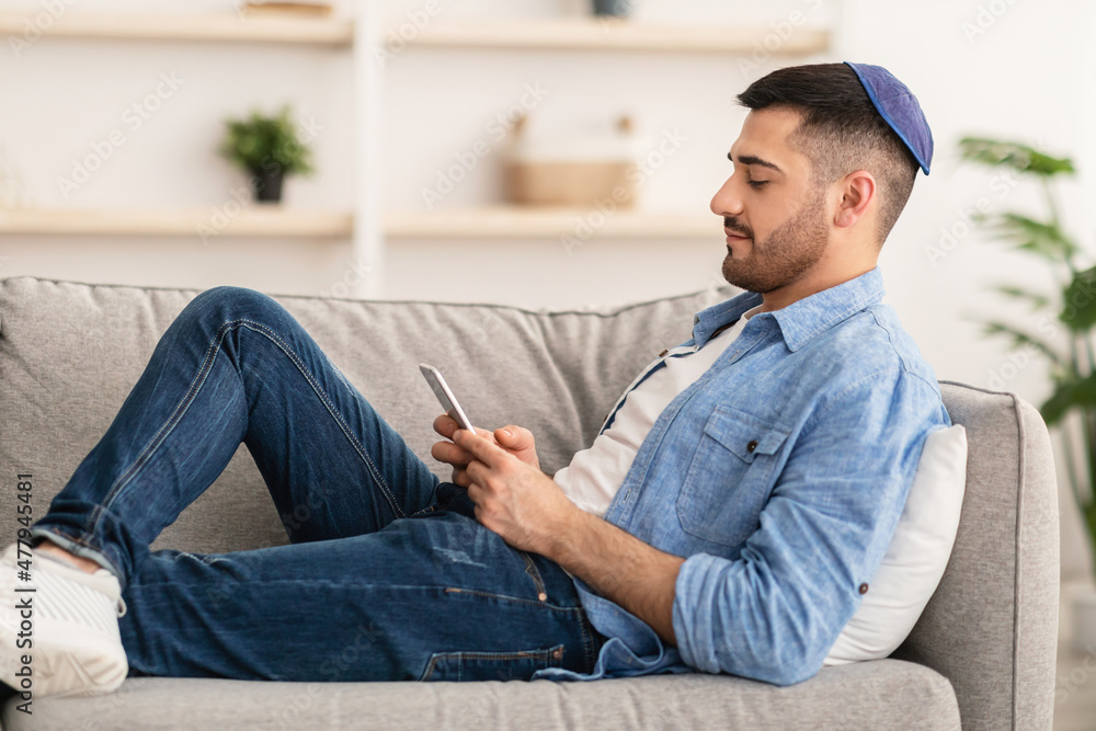 Profile of jew man using mobile phone sitting on couch