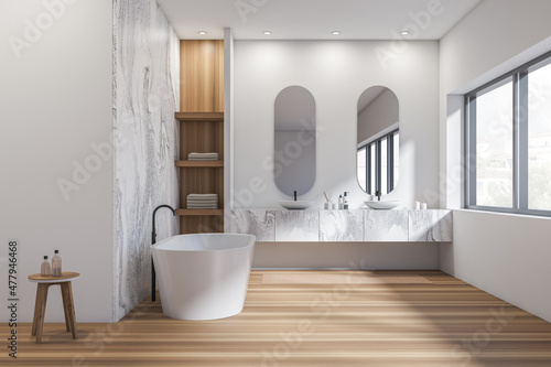 Bright bathroom interior with two sinks, bathtub, oval mirrors, window