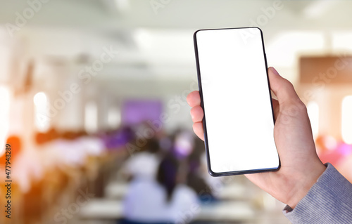 Smart mobile phone which has blank touchscreen holding in hand with blurred big meeting room background, concept for using smart mobile phone with online transactions.