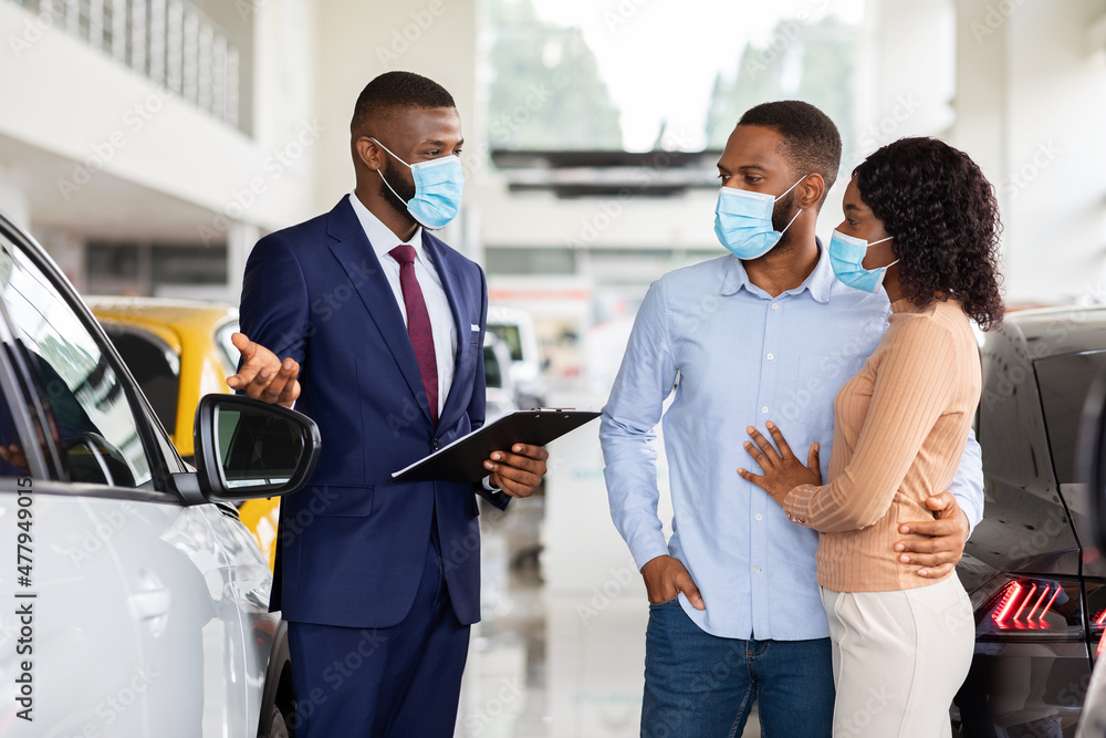 Salesman In Medical Mask Helping Spouses To Choose Car In Dealership Center Salesman In Medical Mask Helping Spouses To Choose Car In Dealership Center