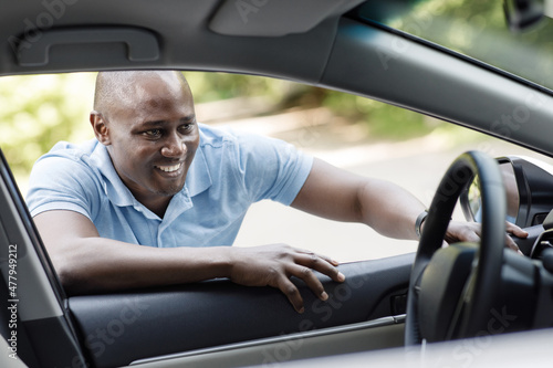 Happy african american man looking inside new car