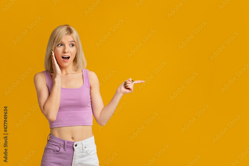 Wow, look there. Shocked young lady pointing finger at empty space standing on yellow background, studo shot Wow, look there. Shocked young lady pointing finger at empty space standing on yellow background, studo shot
