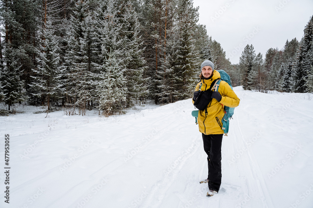 A man walks through the woods with a hiking backpack. Panoramic view of landscape. Survival in the wild. Bright winter equipment Walking in the winter season