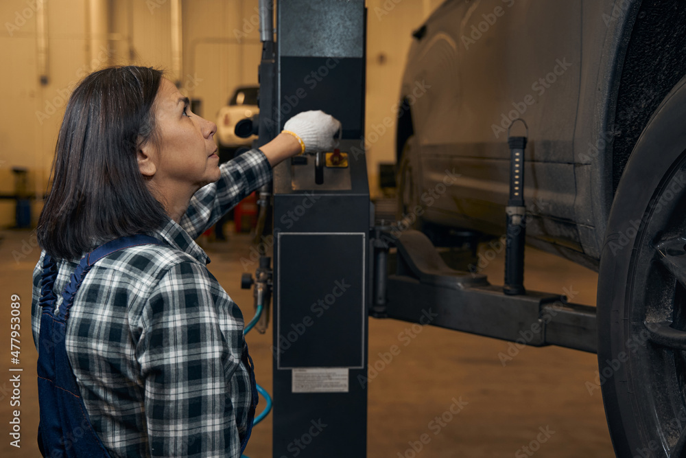Focused lady using special equipment to lift car up