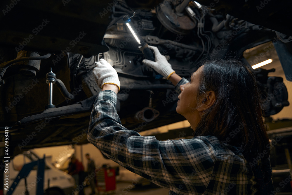Focused woman checking mechanisms of a vehicle under lamp light