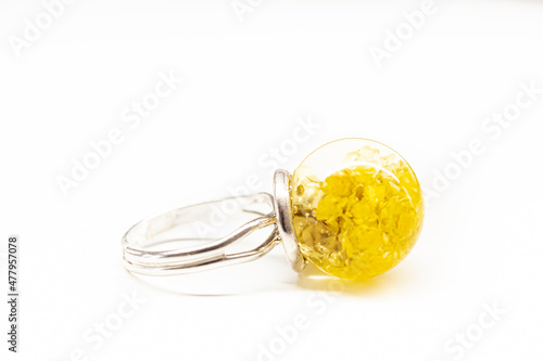 Silver ring with yellow flowers. Dried natural immortelle plants inside transparent sphere shaped epoxy resin ball. Selective focus on the details  blurred background.