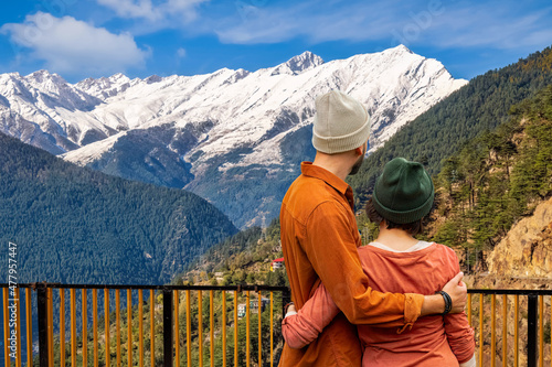 Tourist couple enjoy scenic Himalayan landscape with view of Kinnaur Kailash mountain range from a view point near Kalpa highway at Himachal Pradesh, India.