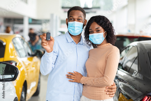 Young African American Spouses In Medical Masks Demonstrating Car Key At Camera