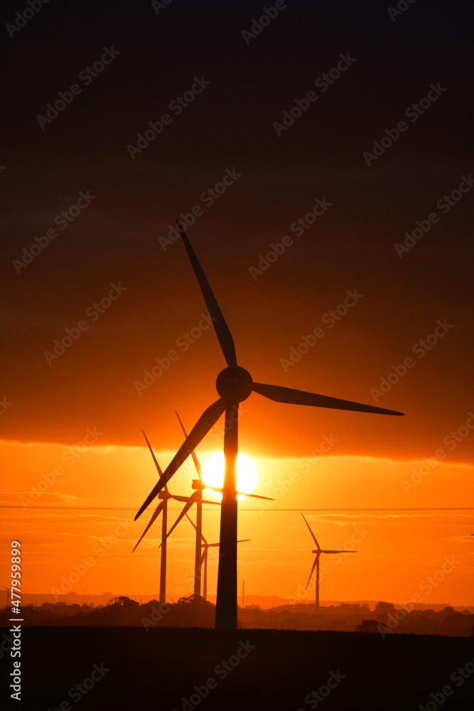 Deep orange sunset falls behind a field of giant wind turbines Deep orange sunset falls behind a field of giant wind turbines