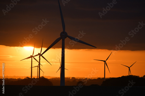 Deep orange sunset falls behind a field of giant wind turbines