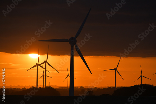 Deep orange sunset falls behind a field of giant wind turbines © Andy
