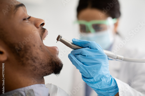 Black Dentist Doctor Lady Using Dental Drill For Male Patient's Teeth Treatment