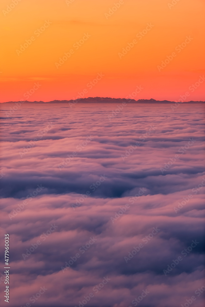 The French and Italian Alps silhouetted against an orange sky above a cloud inversion viewed from Corsica at sunset