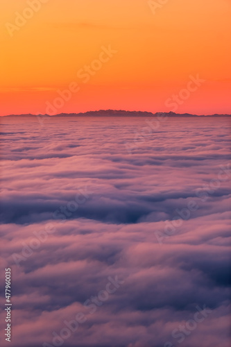 The French and Italian Alps silhouetted against an orange sky above a cloud inversion viewed from Corsica at sunset