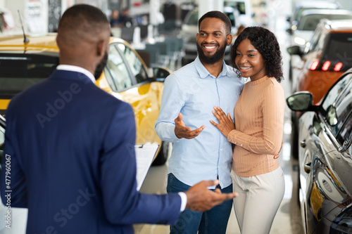 Young Black Couple Talking To Salesman In Dealership Office While Buying Car