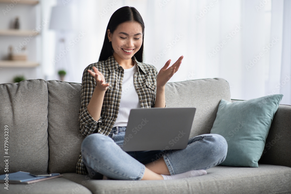 Naklejka premium Pretty young asian lady sitting on couch with laptop