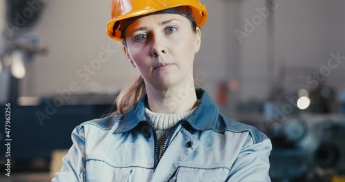 An industrial worker in a hard hat smiles as he walks through a heavy industry manufacturing facility. In the background are various details of a steel structure project.