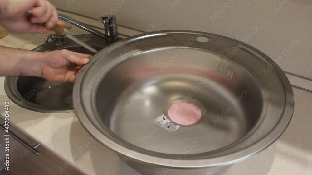 A man's white hand cleans metal burrs with a file from the edge of a new stainless steel kitchen sink A man's white hand cleans metal burrs with a file from the edge of a new stainless steel kitchen sink