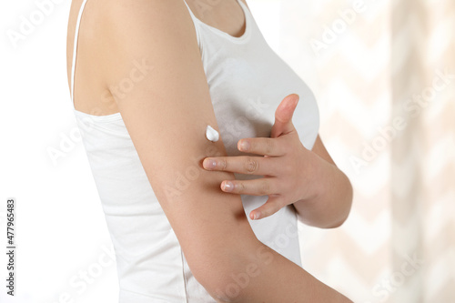 Woman applying lotion and body cream on her arm with dry skin in winter by the window where the sunlight comes in