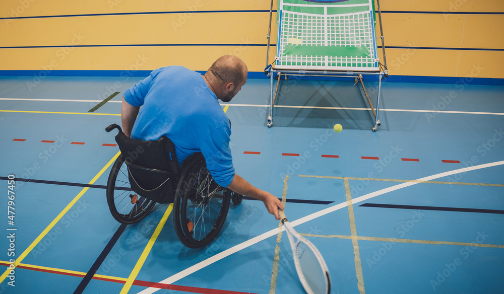 Naklejka premium Adult man with a physical disability who uses wheelchair playing tennis on indoor tennis court