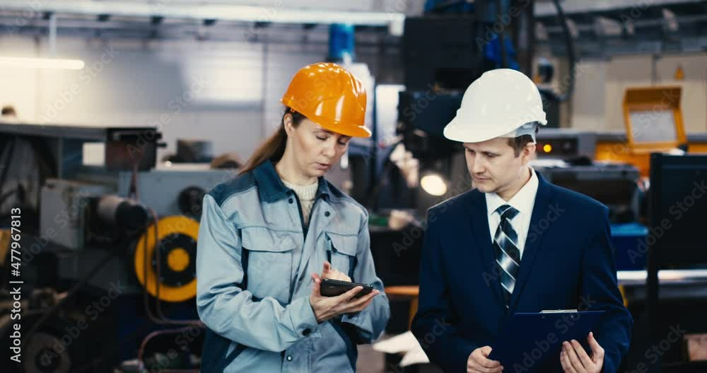 A portrait of an industrial man and woman engineer with tablet in a factory, working. A portrait of an industrial man and woman engineer with tablet in a factory, working.