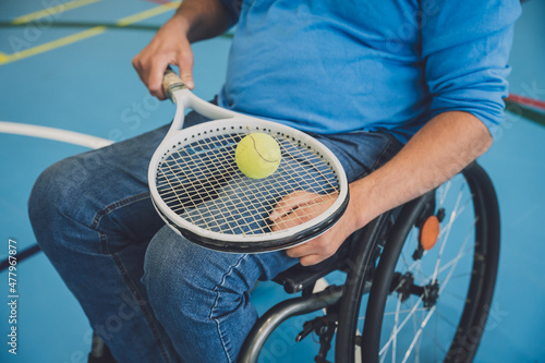Adult man with a physical disability who uses wheelchair playing tennis on indoor tennis court © romaset
