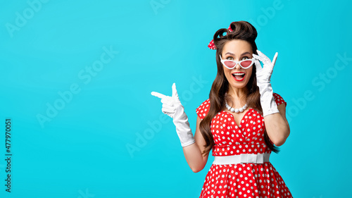 Omg, cool offer. Excited young pinup lady pointing at free space over blue studio background, banner design photo
