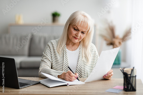 Focused mature woman writing and holding document at home